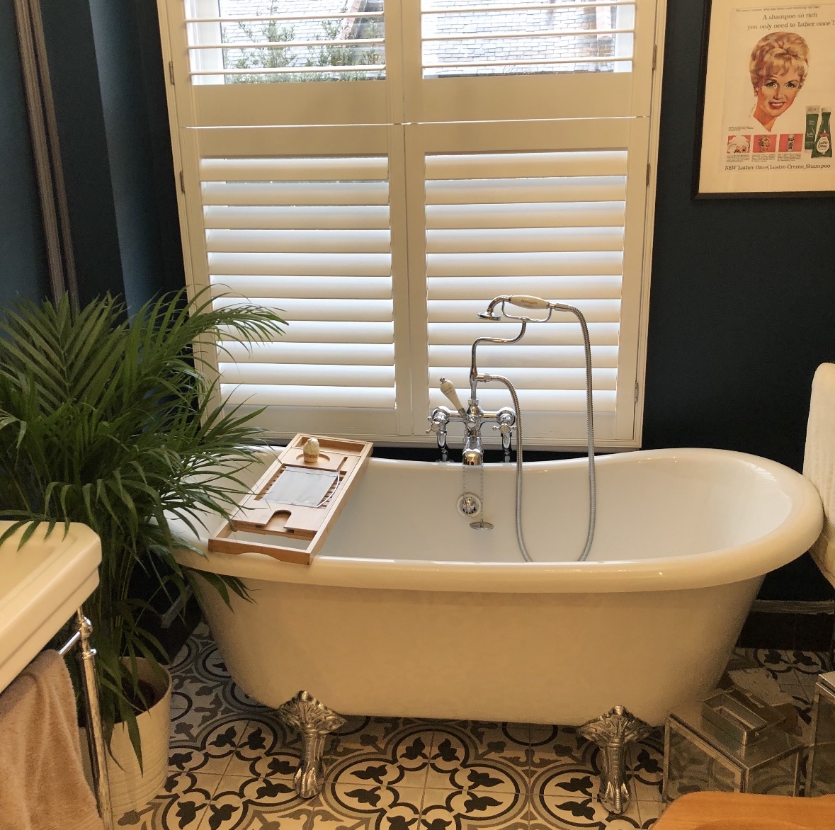 Freestanding roll-top bath with patterned floor tiles and plantation shutters